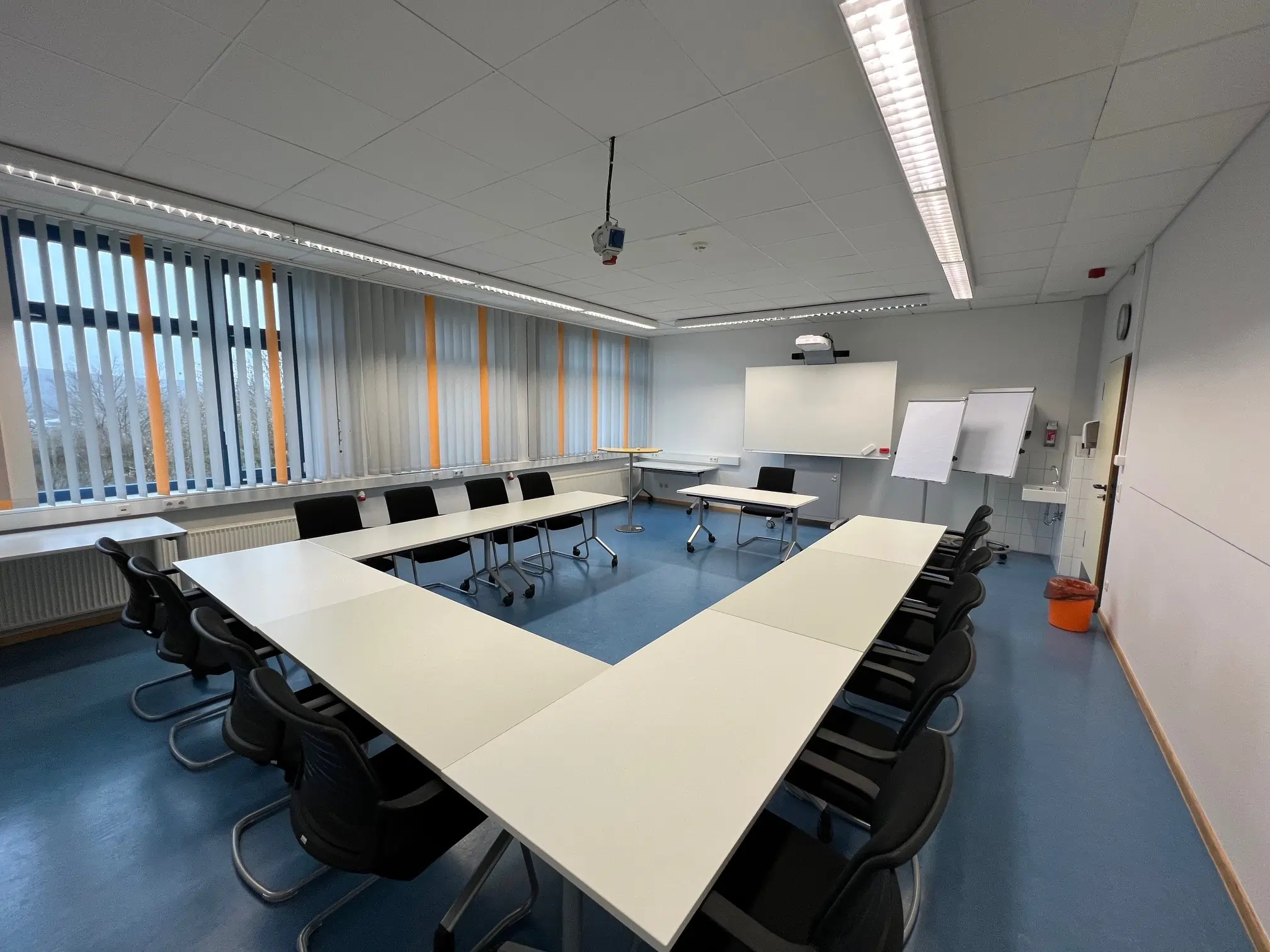 InnovationsRaum. Tagungsraum im Hotel Fünf10 mit Block Form Bestuhlung und einem Stehtisch. An der Wand hängt ein digitales Whiteboard. In der rechten Ecke stehen 2 Flipcharts