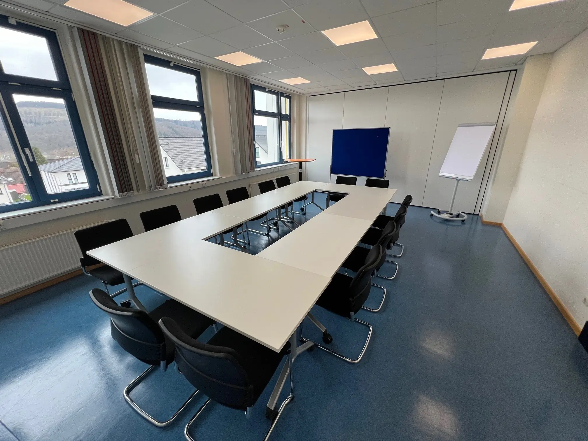 KreativRaum. Tagungsraum im Hotel Fünf10 mit Block Form Bestuhlung und einem Stehtisch. An der Wand steht eine blaue Pinnwand und ein Flipchart. Ein Stehtisch steht in der linken Ecke des Raumes