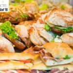 Verschiedene frische belegte Brötchen mit Salat, Käse und Aufschnitt auf einem Buffet, im Hintergrund das Logo des Hotels Fünf 10
