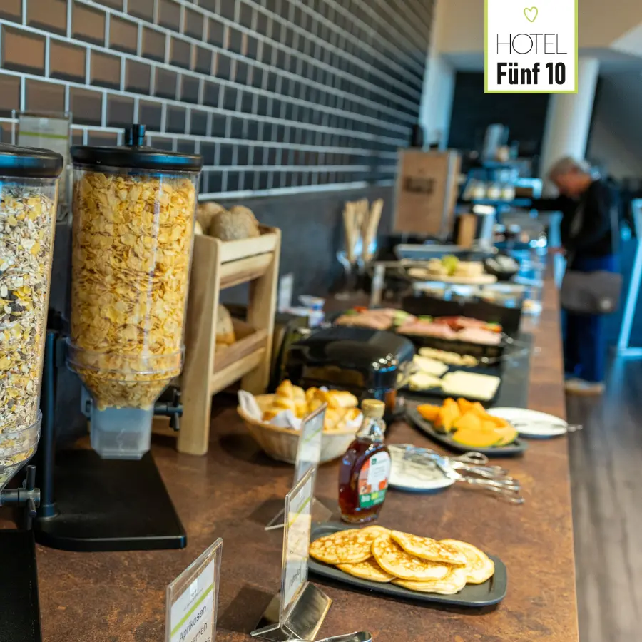 Frühstücksbuffet im Hotel Fünf10 mit Cerealien, Obst, Pancakes und Aufschnitt.